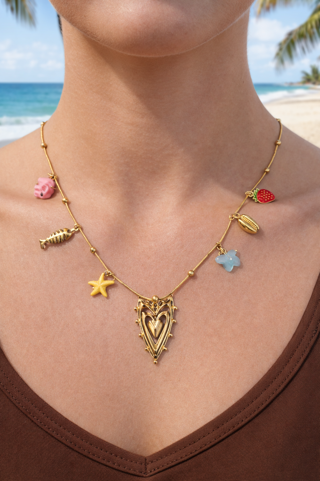 Gold necklace with colorful charms worn by a person on a beach.