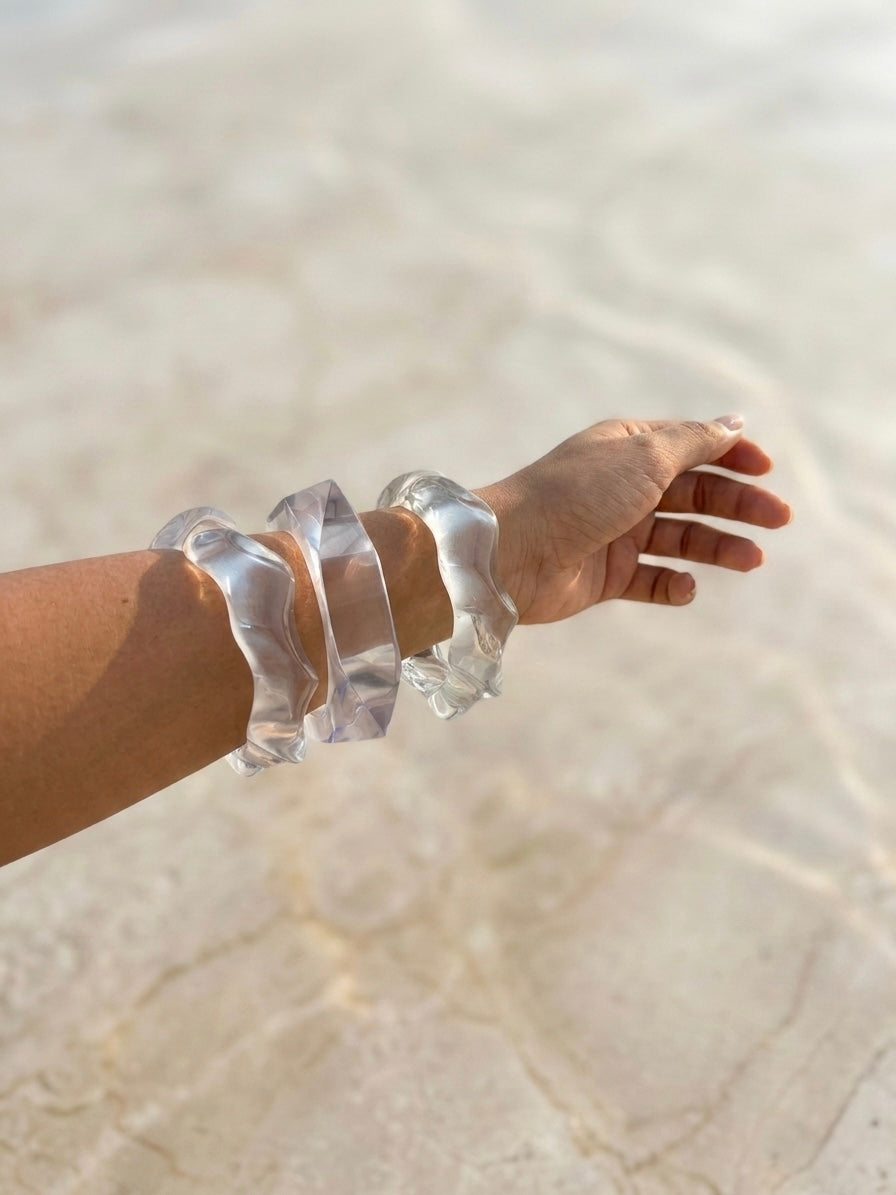 Hand wearing clear bracelets on a sandy background