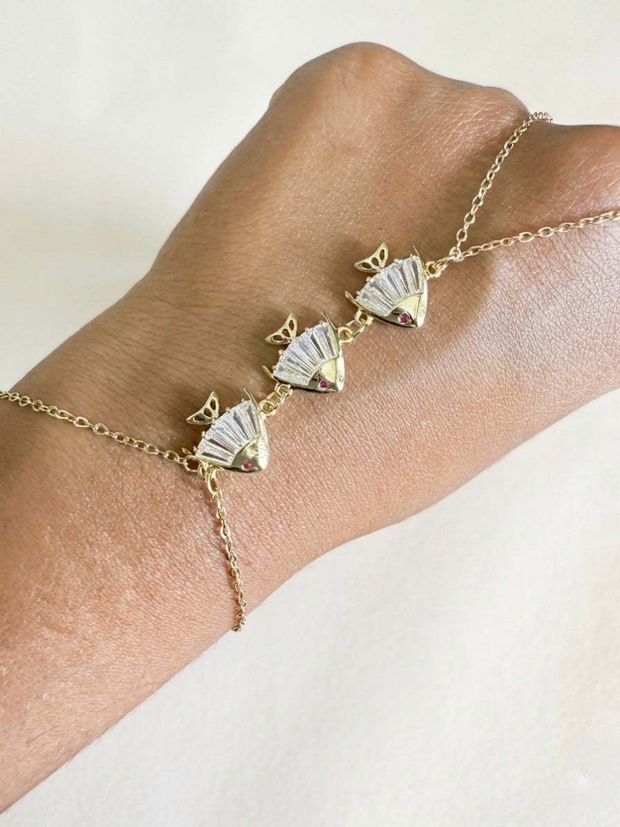 Gold bracelet with fan-shaped charms on a wrist against a neutral background