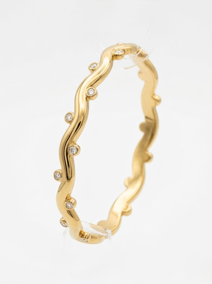Gold bracelet with wavy design and embedded stones on a white background