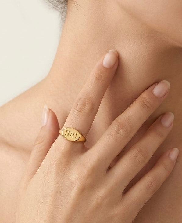 Gold ring with engraved text on a hand against a neutral background