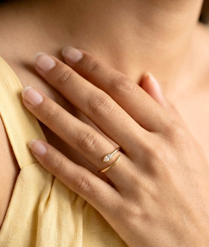 Close-up of a hand wearing a gold ring with a diamond on a light-colored fabric background