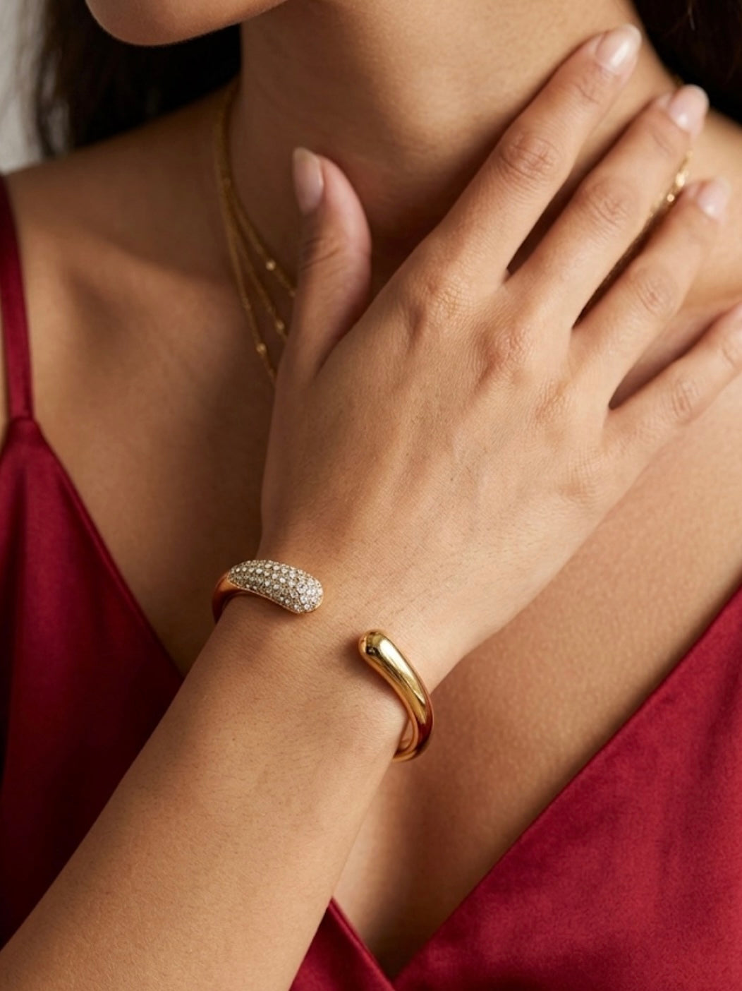 Close-up of a person wearing gold jewelry including a bracelet and ring, with a blurred background.