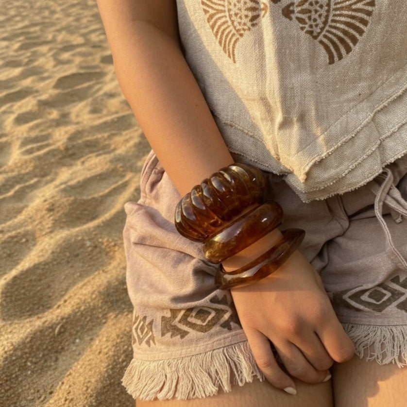 Person wearing a patterned top and shorts with a sandal on a sandy surface