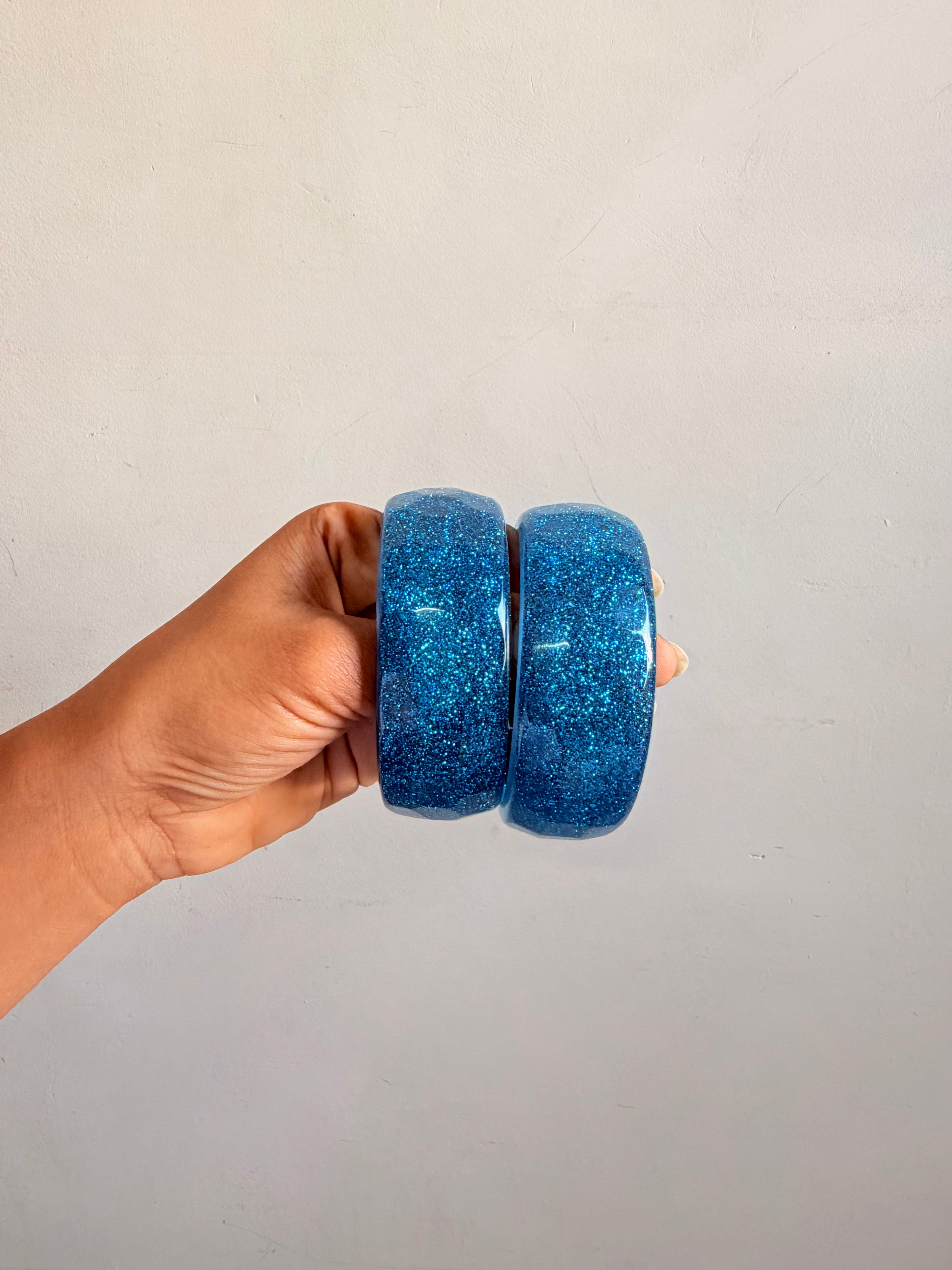 Hand holding two blue glittery bangles against a plain background