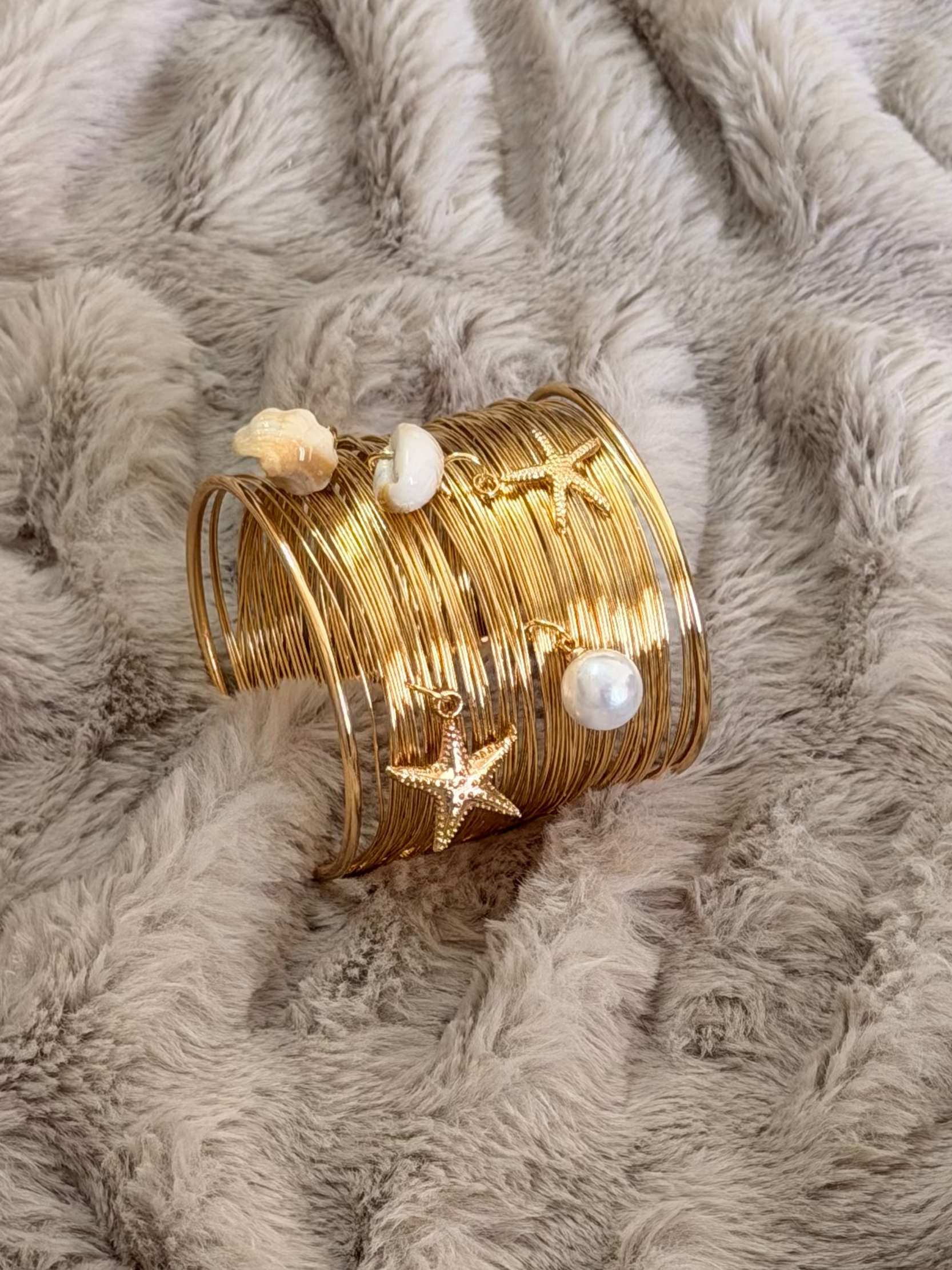 Gold bracelet with star and pearl details on a textured beige surface