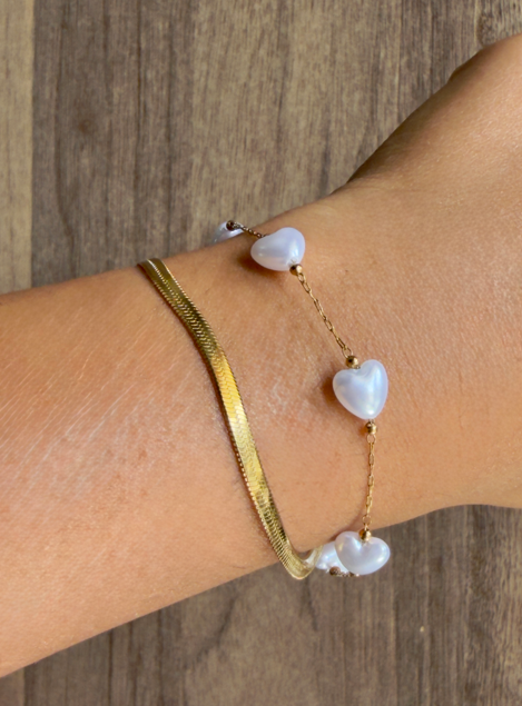 Gold bracelet with heart-shaped pearls on a wrist against a wooden background